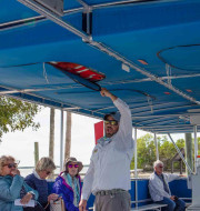 Tour guide standing out boat showing passengers the life vests storage above their heads