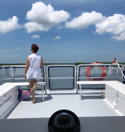 Women with short dark hair and white shirt standing at the bow of boat looking out at the water